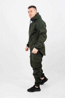 Kendine güvenen biri şık atletik giysiler içinde, modaya uygun bir görünüm sergiliyor. Aydınlık ortam, sakin bir günde kıyafetin tasarımı ve bireyselliğini vurguluyor..