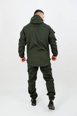 Gösterişli, koyu renk elbiseli bir adam sırtı seyirciye dönük duruyor. Modern stüdyo, şehir tarzını zahmetsizce yakalayan sade bir arkaplan karşısında şık görünümünü ön plana çıkarıyor..