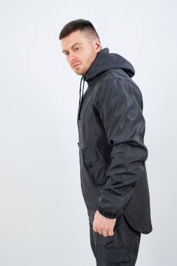 Süslü, siyah bir elbise içinde kapüşonlu ceketi olan bir adam gururla durur. Temiz zemin onun moda ifadesini vurguluyor, onu çağdaş tarzın çarpıcı bir portresi yapıyor..