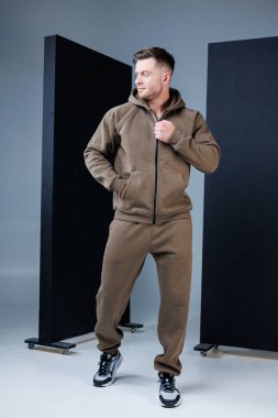 Kendine güvenen bir model modern bir stüdyoda şık kahverengi bir eşofman giyip tarzla konforu harmanlıyor. Atmosfer canlı ve sanatsal, modern modanın altını çiziyor..