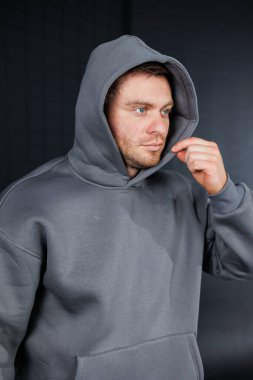 Modaya uygun, minimalist bir mekânda yansıyan gri kapüşonlu bir adam kapüşonunu incelikle düzeltiyor, bir anlık tefekkür ve gündelik bir tarz sergiliyor..