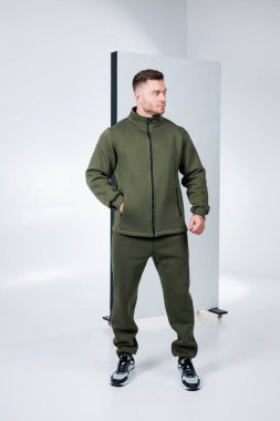 Kendine güvenen bir fitness modeli şık bir stüdyoda duruyor, şık zeytin rengi aktif giysiler giyiyor. Minimalist arka plan dinamik kıyafete ve güçlü duruşa odaklanmamızı sağlar..
