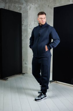 Modaya uygun bir adam moda bir stüdyoda şık spor ayakkabılarla eşleştirilmiş donanma eşofmanını sergiliyor. Yumuşak ışık uzayın serin atmosferini arttırır.