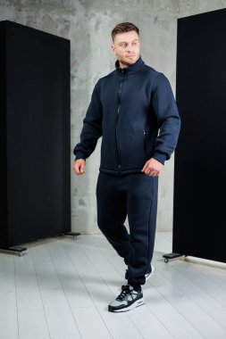 Bir adam şık bir donanma spor kıyafetinin içinde şık bir şehir stüdyosunda modern bir görünüm sergiliyor. Basit arka plan moda seçimini vurguluyor..