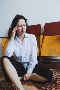 Genç bir kadın, rahat bir şekilde, rahat bir şekilde yerde oturuyor. Rahat bir şekilde, elini yüzüne koyuyor. Huzurlu ve huzurlu bir ev ortamının tadını çıkarıyor.