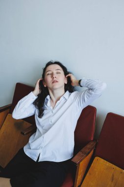 Gıcır gıcır beyaz gömlekli ve siyah şortlu genç bir kadın sıradan bir şekilde bir sandalyeye oturur ve basit, modern bir uzay boşluğunda bir anlık iç gözlem yapar.