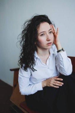 Huzurlu bir ortamda, kıvırcık saçlı, şık beyaz bir gömlek giyen genç bir kadın duygularını derinden yansıtıyor, içsel gözlem ve zihinsel berraklığı teşvik ediyor.