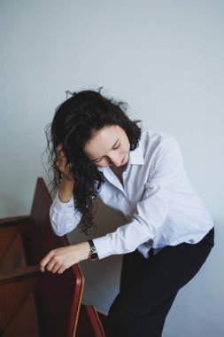 Resmi bir gömlek giymiş genç bir kadın, nazikçe bir merdivene yaslanırken düşünceli görünür. İç gözlem ve içsel düşüncelerle dolu bir anı nazikçe yakalar.