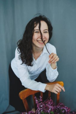 Neşeli genç bir kadın güzel bir çiçek buketiyle poz veriyor yumuşak, pastel bir ortamda, canlı ruhunu vurguluyor ve anı özel kılıyor.