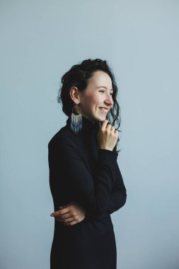 Şık siyah balıkçı yakalı bir kadının çarpıcı portresi zarif küpelerini ve ışıltılı gülümsemesini minimalist bir ortamda sergiliyor zarafet ve güven saçıyor.