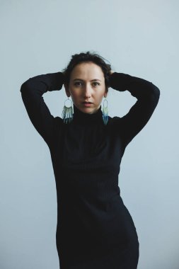 Kendine güvenen bir mankende kalın küpeleri olan şık siyah bir kıyafet sergileniyor, genel görünüm ve titreşimi arttıran minimum arkaplan karşısında çarpıcı bir kontrast oluşturuyor.