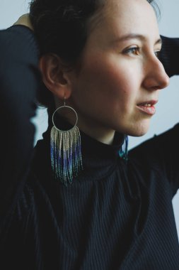 Zarif bir şahıs zarif bir şekilde poz verir, güzel, sallanan küpeleri yumuşak, nötr bir arka plana vurgular. İfadesi özgüven ve özgüven saçıyor..