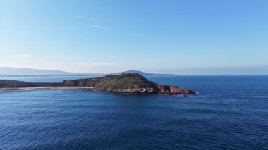 Berrak mavi gökyüzü berrak okyanusla buluşuyor yemyeşil bir ada uzakta gururla duruyor doğal güzellik ve sakinlikle dolu huzurlu bir manzara yaratıyor..