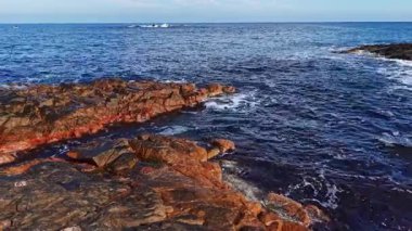 Bu sahne, pürüzlü kayaların gün batımında sakin ve parıldayan sularla buluşup huzur ve doğal güzelliği çağrıştıran çarpıcı bir kıyı bölgesini gösteriyor..