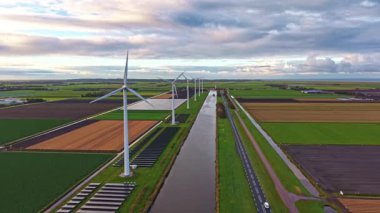 Görkemli rüzgar türbinleri yavaşça dönerek kırsal alanda temiz enerji yaratırlar. Bereketli tarlalar ve dolambaçlı bir kanal akşam gökyüzünü yansıtıyor, doğanın güzelliğini şehrin dışında sergiliyor..