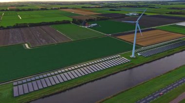 Geniş alanlar, yüksek rüzgar türbininin yanındaki sıra sıra güneş panelleri ile modern yenilenebilir enerji donanımını sergiliyor..