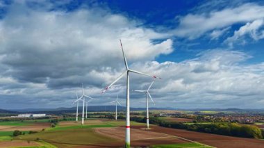 Uzun rüzgar türbinleri rüzgarda zarifçe döner, canlı tarlalara ve uzak tepelere karşı kurulur, güneşli bir öğleden sonra yenilenebilir enerjinin güzelliğini gösterir..