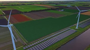 Yüksek rüzgar türbinleri ve güneş panelleri içeren nefes kesici manzaralar yemyeşil alanlar, canlı renkler ve gün batımının altın saatinde dingin bir kanal ile uyumlu..