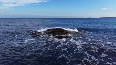 Parlak güneş ışığı sakin denizden yansıyor dalgalar yavaşça karanlık kayalara vururken. Ufuk her yere yayılıyor, kıyı manzarasının manzaralı güzelliğini gözler önüne seriyor..