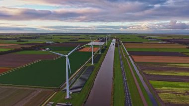 Uzun rüzgar türbinleri, hava kararırken yeşil ve kahverengi alanlar arasında huzurlu bir kanal oluşturarak, huzurlu bir manzaradaki yenilenebilir enerjinin güzelliğini yansıtıyor..
