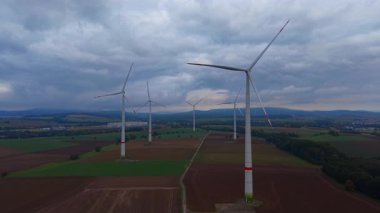 Dev rüzgar türbinleri açık alanlarda dik durur ve temiz enerji üretirken yavaşça dönerler. Huysuz bir gökyüzü, yumuşak bir öğleden sonra ışığı altında yeşil ve kahverengi manzaraya zıtlık katar..