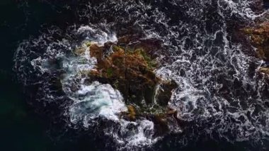 Dalgalar engebeli kayalarla çarpışırken su kükrer ve havaya püskürtür. Sahne, okyanusun hareketli enerjisini ve hareketini dramatik bir zemin üzerinde yakalıyor..