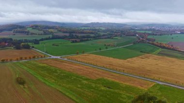 Yeşil yemyeşil tarlalar ve altın saman araziyi kaplıyor, dolambaçlı yollar ve uzak tepeler bulutlu bir sonbahar gününün sükunetini yakalıyor..