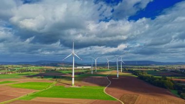 Geniş bir kırsalda, rüzgâr türbinleri zarifçe dönerek rüzgardan gelen enerjiyi yakalar, bereketli alanlar ve görkemli gökyüzü, doğayı ve teknolojiyi uyum içinde gösterir..