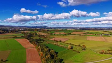 Renkli tarlalar tüm ülkeye yayılmış, zengin yeşiller, sıcak kahverengiler ve altın sarısı renkler sergileniyor. Gökyüzü parlak mavi, beyaz bulutlarla benekli, uzak tepeler ise manzaralı bir zemin..