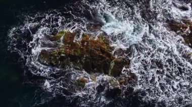 Dalgalar dalgaların oluşturduğu bir kaya kümesini çevreleyerek dramatik bir deniz manzarasına karşı köpük ve suyu harmanlıyor..