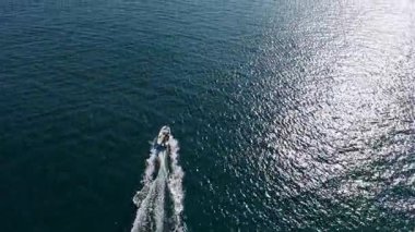 Bir tekne sakin mavi sularda pürüzsüz bir şekilde hareket eder. Güneş ışığı yüzeyde parıldarken hafif dalgalanmalar yaratır. Sahne, sahilde huzur ve maceranın özünü yakalıyor..