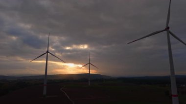 Rüzgar türbinleri çarpıcı bir siluet oluşturur. Güneş batarken çarpıcı bir gökyüzüne karşı. Manzara boyunca yumuşak bir ışık yayar. Doğa ve teknoloji bu huzurlu sahnede uyum içinde..