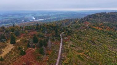 Kapsamlı bir manzara, dalgalı tepeler boyunca canlı sonbahar renklerini gözler önüne seriyor. Ağaçların arasından geçen huzurlu bir patika ve uzaktaki sisli ufuklar doğa uyanıyor..