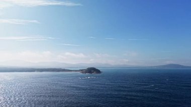 Ufuk boyunca uzanan engin mavi sular, kıyıya vuran hafif dalgalarla. Huzurlu denizin ortasında yükselen uzak adalar sakin ve sakin bir atmosfer yaratıyor..
