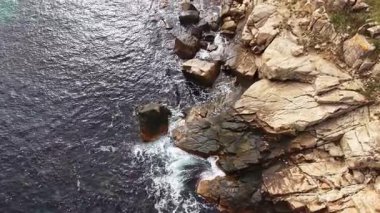 Dalgalar kayalık kıyıya vurduğunda parlak güneş ışığı suda dans eder. Uçurumlar dik bir şekilde yükseliyor, doğanın vahşi güzelliğini denizle mükemmel bir uyum içinde gösteriyor..