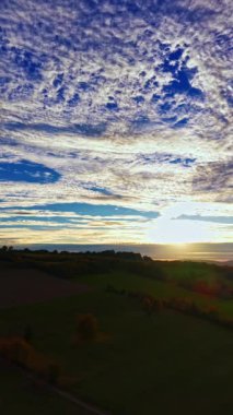 Güneş tepelerin ardında batarken bulutlar turuncu ve pembe tonlarını yansıtıyor ve doğal güzellik ve sükunetle dolu çarpıcı bir akşam sahnesi yaratıyor..