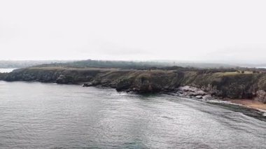 Sisli bir sabah, kıyıya vuran dalgaların yanında engebeli kıyı kayalıklarını ortaya çıkarıyor. Yumuşak güneş ışığı bulutları delip geçer ve yansıma için mükemmel bir atmosfer yaratır..