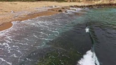 Yumuşak dalgalar, altın kumların köpüklü suyla buluştuğu sakin bir plaja yuvarlanıyor. Güneş batmaya başlıyor, denizi yansıtan sıcak renklerle gökyüzünü boyuyor..