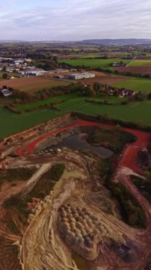 Kuş bakışı perspektif, canlı yeşillik ve kırsal manzarayla çevrili kırmızı toprakla çevrili aktif bir inşaat alanını vurgular, değişen dünyanın güzelliğini yakalar..