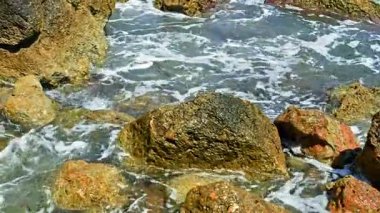 Deniz dalgaları kayalara çarptıkça köpük oluşturur. Kristal mavi suyu olan kayalık okyanus kıyısı. Sudaki kayalar.