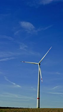 Mavi gökyüzüne karşı yel değirmenlerinin dikey videosu. Rüzgar türbinleri bir alanda dönüyor ve enerji üretiyor. Alternatif enerji üretimi.