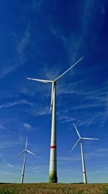Mavi gökyüzüne karşı yel değirmenlerinin dikey videosu. Rüzgar türbinleri bir alanda dönüyor ve enerji üretiyor. Alternatif enerji üretimi.
