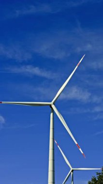 Mavi gökyüzüne karşı yel değirmenlerinin dikey videosu. Rüzgar türbinleri bir alanda dönüyor ve enerji üretiyor. Alternatif enerji üretimi.