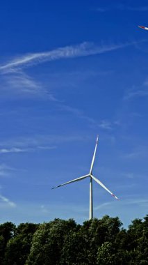 Bir çiftlikte rüzgar türbinleri çevre dostu bir elektrik santralinde yenilenebilir elektrik üretiyor. Mavi gökyüzüne karşı yel değirmenleri.