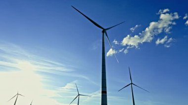 Mavi gökyüzüne karşı bir rüzgar türbini alanı. Rüzgar türbinleri inanılmaz güzel bulutları olan bir gökyüzüne doğru dönerek enerji üretir..