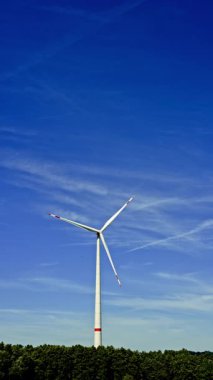 Bir çiftlikte rüzgar türbinleri çevre dostu bir elektrik santralinde yenilenebilir elektrik üretiyor. Mavi gökyüzüne karşı yel değirmenleri.