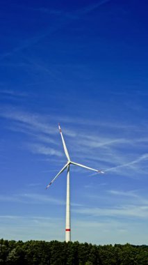 Bir çiftlikte rüzgar türbinleri çevre dostu bir elektrik santralinde yenilenebilir elektrik üretiyor. Mavi gökyüzüne karşı yel değirmenleri.