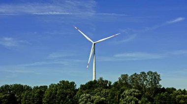 Büyük, güçlü bir yel değirmeni enerji üreten bir alanda dönüyor. Yel değirmenleri tarafından üretilen yeşil enerji. Mavi gökyüzü arka planında rüzgar türbini