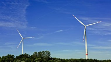 Rüzgâr türbininin parlak mavi gökyüzüne karşı dağınık bulutlu videosu. Yenilenebilir enerji yel değirmenleri tarafından üretilir. Mavi gökyüzüne karşı uzun yel değirmenleri.