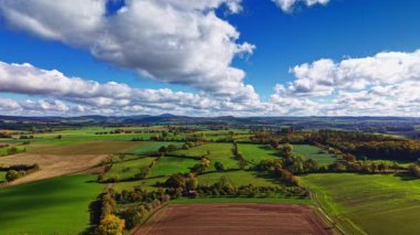 Çarpıcı kırsal alan, doğanın sükunetini gösteren tüylü bulutlarla dolu büyüleyici mavi gökyüzünün altında yemyeşil tarlalar ve altın topraklar barındırıyor..